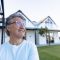 Smiling caucasian senior man wearing eyeglasses looking away against house in yard, copy space. Unaltered, contemplation, support, assisted living and retirement home.